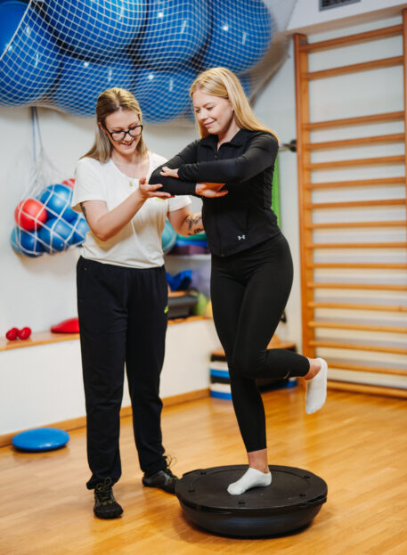 Skupinske vadbe za hrbtenico – Fizioterapija Rudolfovo 3 Skupinska vadba za hrbtenico – fizioterapevtka pomaga pacientki pri vadbi ravnotežja | Fizioterapija Rudolfovo